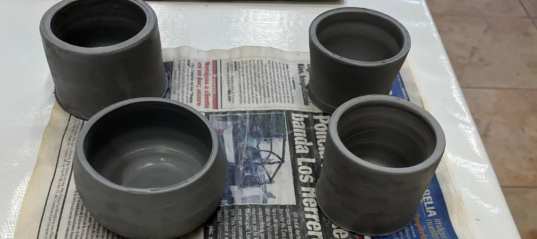 Cuatro vasos de barro gris sobre papel periódico