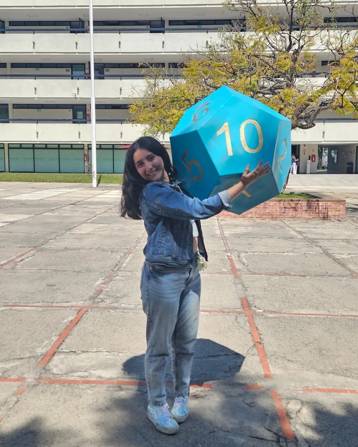Diseñadora sosteniendo un dado azul gigante al aire libre